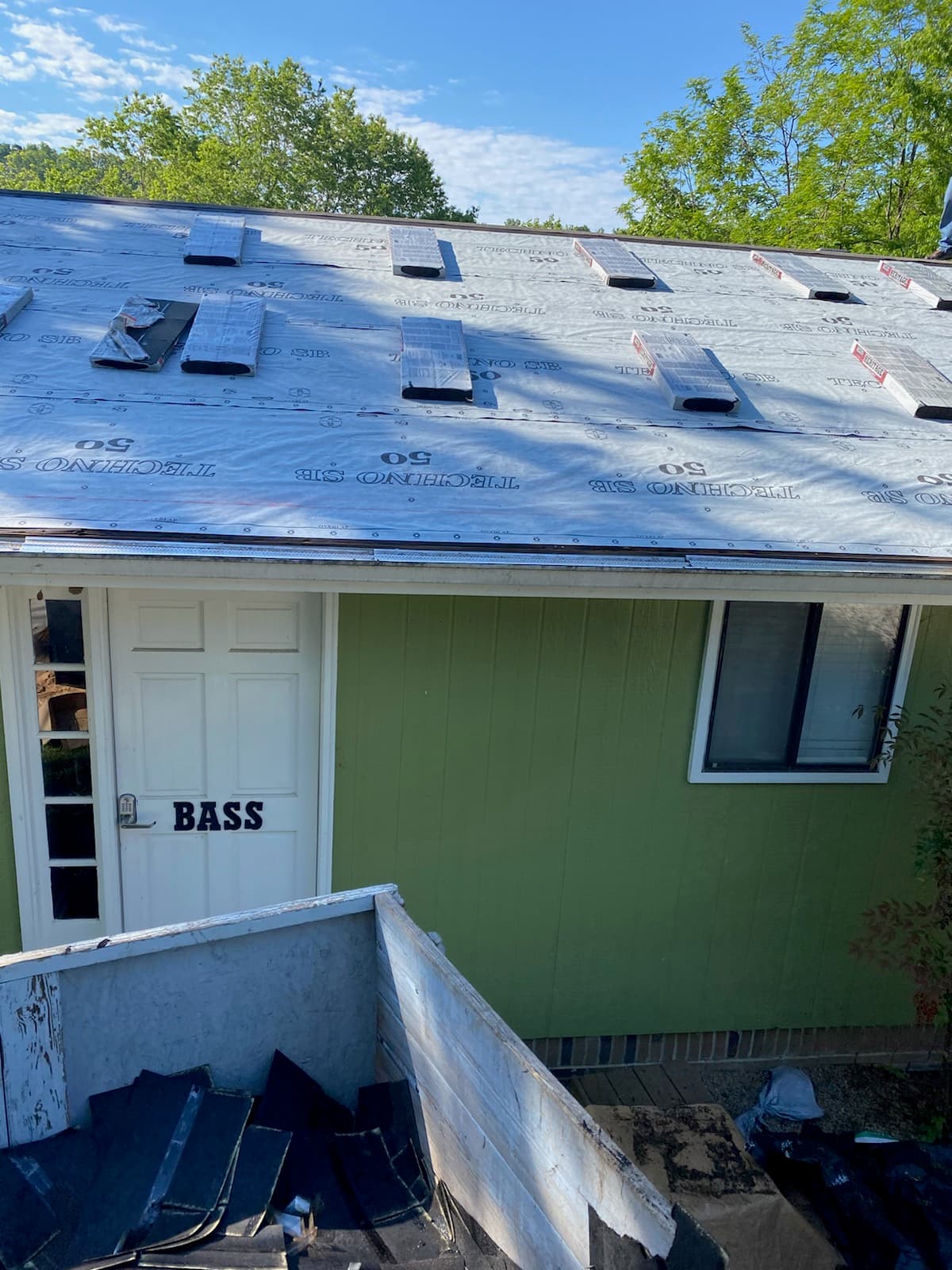 Roof replacement underway with underlayment installed and debris trailer below